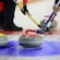 3 curling stones with curlers sweeping the ice